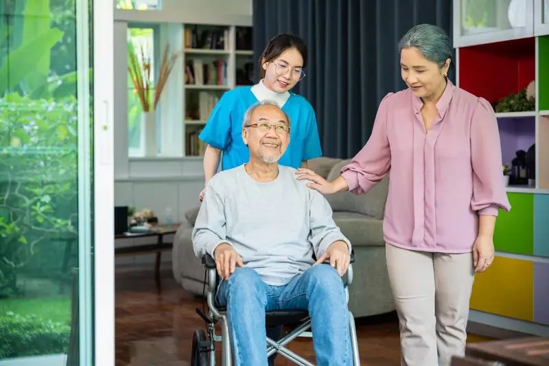 Carer supporting client in wheelchair alongside family